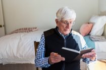 Uomo anziano che legge un libro nella sua camera da letto — Foto stock