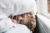 Garçon de 6 ans au lit avec des couvertures sur la tête — Photo de stock