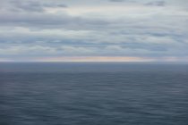 Movimento turvo abstrato do oceano, horizonte e céu tempestuoso ao entardecer — Fotografia de Stock
