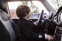 6-летний мальчик сидит в машине, держа руль — стоковое фото