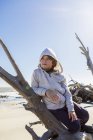 Menino de seis anos em uma praia apoiada em um tronco de árvore de madeira à deriva — Fotografia de Stock