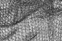 Inverted black and white image of commercial fishnets and ropes on a fishing quay. — Stock Photo