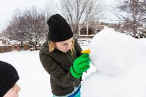 Девочка-подросток и её младший брат строят снеговика в саду — стоковое фото