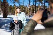 Mother taking a picture of her two children, a boy and teenage girl in snowy forest landscape. — Stock Photo