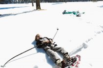 Six year old boy wearing snow shoes, lying down on his back in snow — Stock Photo