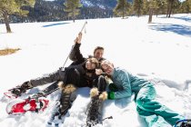 Eine Frau und ihre beiden Kinder, ein Mädchen im Teenageralter und ein kleiner Junge liegen in Schneeschuhen und Skiausrüstung im Schnee. — Stockfoto