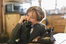 Menino de seis anos de idade em um terno e gravata falando em um telefone vintage velho em casa — Fotografia de Stock