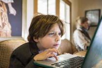 Enfocado niño de seis años escribiendo en una computadora portátil en casa - foto de stock