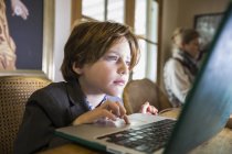 Enfocado niño de seis años escribiendo en una computadora portátil en casa - foto de stock