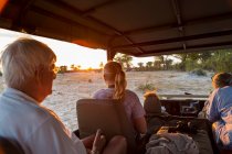 Tre generazioni di una famiglia al safari, in un veicolo al tramonto. — Foto stock