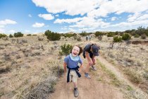 Bambino di sei anni che corre su un sentiero escursionistico con la sorella maggiore, bacino del Galisteo, NM. — Foto stock
