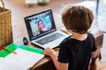 Uma criança trabalhando em casa, olhando para o professor na tela aulas on-line durante o confinamento — Fotografia de Stock