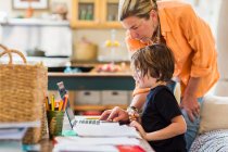 Mulher adulta ajudando seu filho de seis anos com uma sessão de aprendizagem remota em um laptop, usando um touch pad. — Fotografia de Stock
