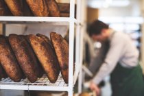 Kunsthandwerker backen spezielles Sauerteigbrot, Regale mit Brot und ein Bäcker im Hintergrund. — Stockfoto