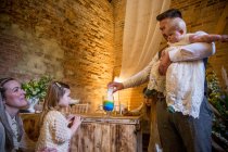 Family pouring coloured sand into glass jar during naming ceremony in an historic barn. — Stock Photo