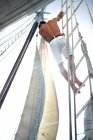 Man in white shorts with bare chest climbing up the rigging of a sailing boat. — Stock Photo