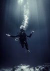 Underwater view of diver wearing wetsuit, diving goggles and oxygen cylinder, air bubbles rising. — Stock Photo