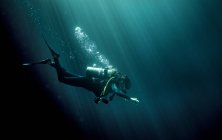 Unterwasser-Ansicht des Tauchers in Neoprenanzug, Taucherbrille und Sauerstoffflasche, Luftblasen steigen auf. — Stockfoto
