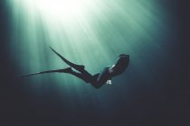 Unterwasser-Ansicht des Tauchers in Neoprenanzug und Schwimmflossen, Sonnenlicht filtert von oben durch. — Stockfoto