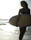 Frau steht an einem Sandstrand am Meer und hält ein Surfbrett. — Stockfoto