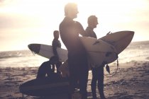 Чотири чоловіки в костюмах, що стоять на піщаному пляжі, несуть дошки для серфінгу . — стокове фото