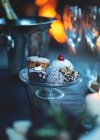 Close up of glass cake stand with a selection of cakes, champagne glasses and wine cooler in the background. — Fotografia de Stock