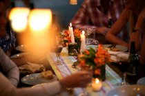 Pessoas sentadas em uma mesa com copos de vinho, pratos, flores e velas. — Fotografia de Stock