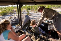 Veículo com duas crianças e um guia turístico inclinado para fora e olhando para a carcaça de um elefante morto. — Fotografia de Stock