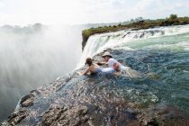 Man and a girl, father and daughter in the water of the Devil's Pool on the edge of Victoria Falls, mist rising from the falling water. — Stock Photo