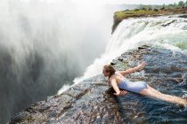 Giovane ragazza in acqua presso la piscina Devils sdraiata sul davanti, braccia aperte, sul bordo della scogliera di Victoria Falls. — Foto stock