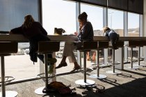 Зріла жінка і двоє дітей сидять на високих табуретках в залі вильоту аеропорту з видом на перон аеропорту . — стокове фото