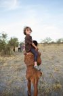 Fünfjähriger Junge reitet auf den Schultern eines San-Buschmanns. — Stockfoto