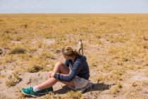 Menina de 12 anos sentada assistindo meerkats emergem de seus entulhos, no deserto de Kalahari. — Fotografia de Stock