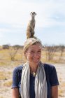 Mujer adulta con suricata en la cabeza, desierto de Kalahari, sartenes Makgadikgadi, Botswana - foto de stock
