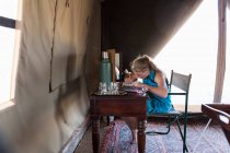 A twelve year old girl sitting at a desk in a tent at a wildlife reserve camp, drawing. — Stock Photo