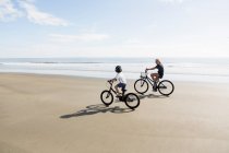 Братья и сестры, мальчик и девочка катаются на велосипеде по пляжу. — стоковое фото