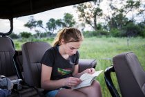 13 ans fille écrit dans son journal assis dans un véhicule sur safari — Photo de stock