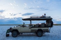 Sei anni ragazzo e la sua sorella adolescente seduto sulla cima di un veicolo safari al tramonto — Foto stock