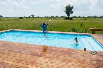 Niño de 6 años saltando a la piscina, campamento de tiendas de campaña, Botswana - foto de stock