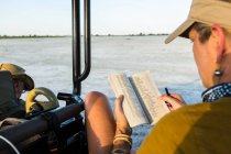 Mujer mirando un libro o diario en un vehículo de safari, Botswana - foto de stock
