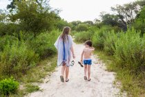 Rear view of teen sister and her brother walking on dirt path, Maun, Botswana — Stock Photo