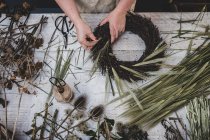Frau bastelt einen kleinen Winterkranz aus getrockneten Pflanzen, braunen Blättern und Zweigen und Samen. — Stockfoto