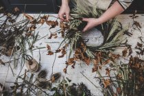 Женщина делает небольшой зимний венок из сушеных растений, коричневых листьев и веток, и саженцев. — стоковое фото