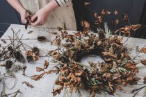 Woman making a small winter wreath of dried plants, brown leaves and twigs, and seedheads. — Stock Photo