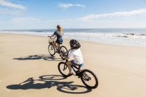 Bambini in bicicletta sulla sabbia vicino all'acqua, un ragazzo e una ragazza. — Foto stock