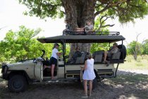 Ein Safari-Fahrzeug parkt im Schatten, sechs Familienmitglieder ruhen. — Stockfoto