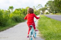Um menino de cinco anos de idade em uma camisa vermelha andando de bicicleta em uma rua residencial tranquila . — Fotografia de Stock