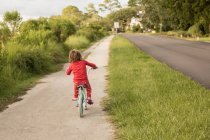 Пятилетний мальчик в красной рубашке катается на велосипеде по тихой жилой улице. — стоковое фото