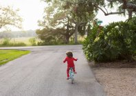 Um menino de cinco anos de idade em uma camisa vermelha andando de bicicleta em uma rua residencial tranquila . — Fotografia de Stock