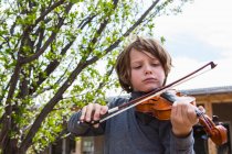 6 year old boy playing violin outside of his home — Stock Photo